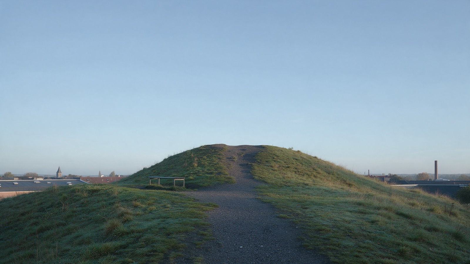 Halde mit Schotterweg unter weitem blauem Himmel, am Horizont ein Schornstein