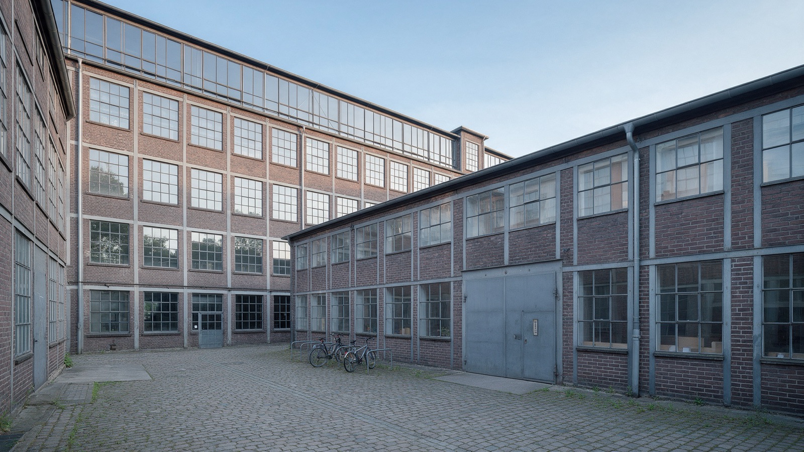 Backsteinhof mit Fahrradständer und grauer Stahltür, oben die großen Fenster des Studios